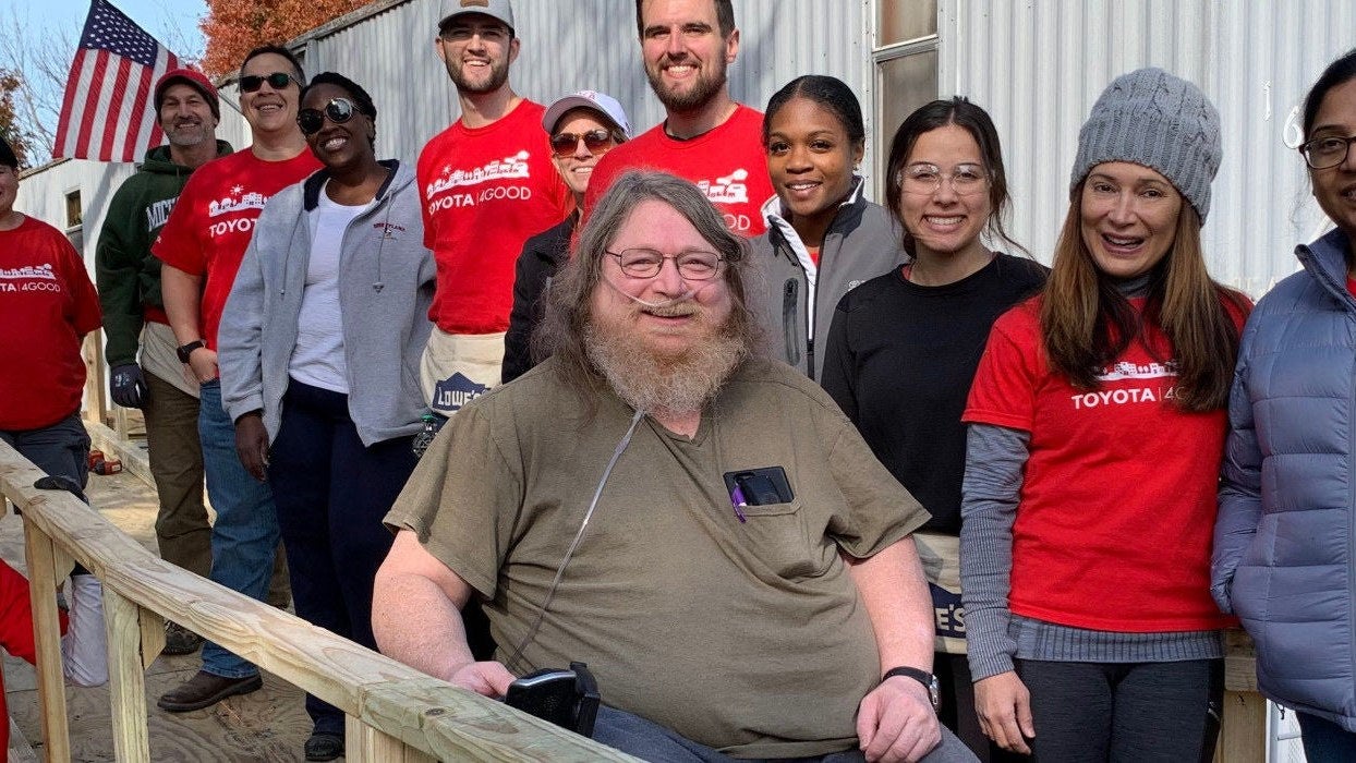 Group of smiling volunteers in red Toyota shirts gathered around a community project